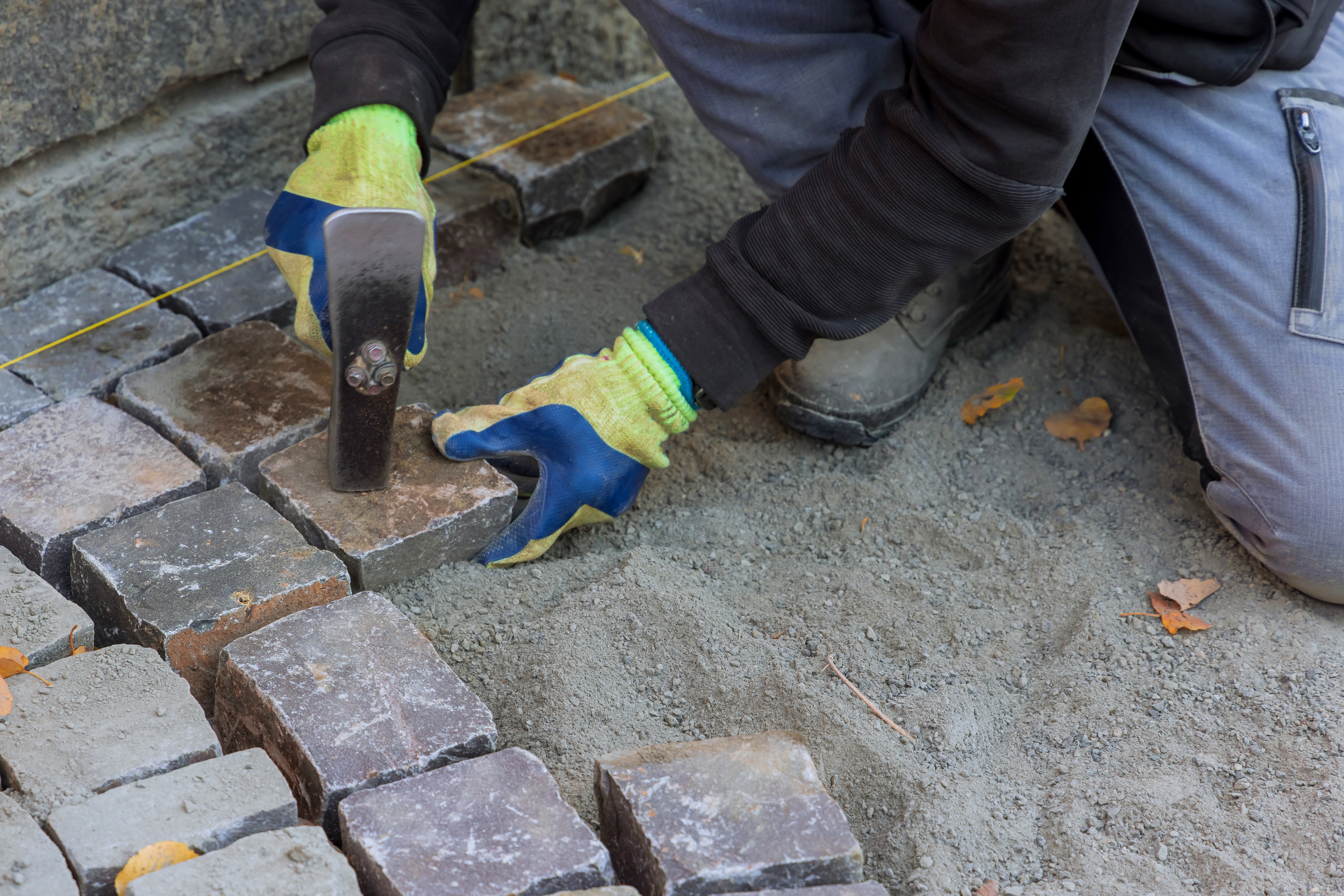 The master in gloves lays paving stones in layers stone road by professional paver worker
